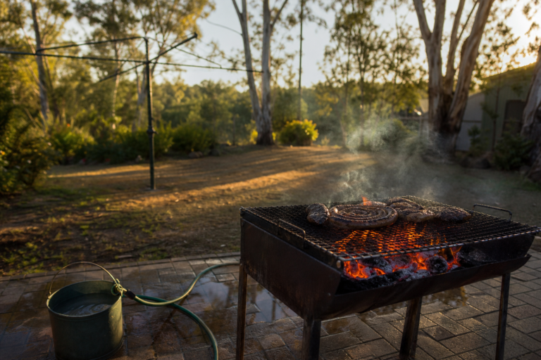Braai fire ban rules in Australia, a charcoal braai fire glowing safely in a cleared Australian backyard in the late afternoon